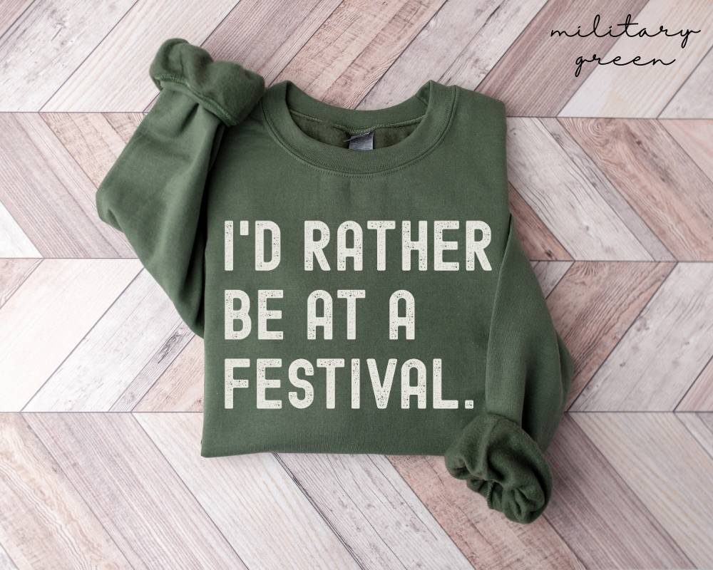 Military green sweatshirt with 'I'd rather be at a festival' text on a wooden floor.