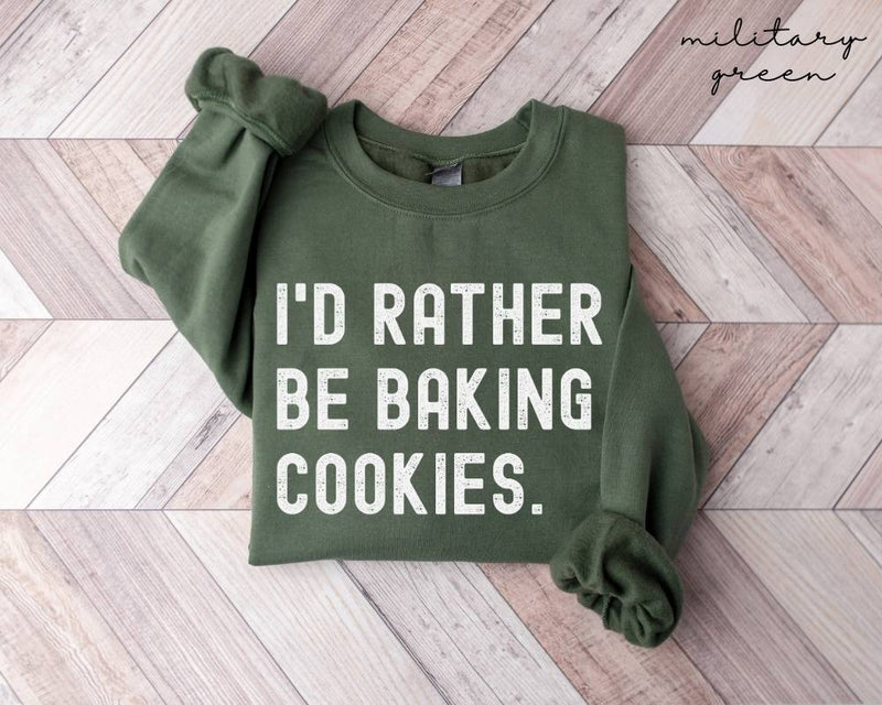 Military green sweatshirt with 'I'd rather be baking cookies' text on a wooden floor.