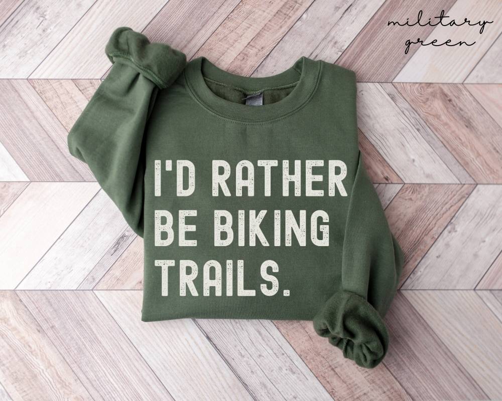 Military green sweatshirt with 'I'd rather be biking trails' text on a wooden floor.