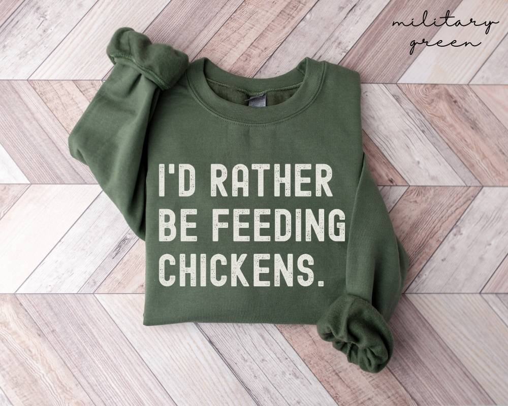 Military green sweatshirt with 'I'd rather be feeding chickens' text on a wooden floor.