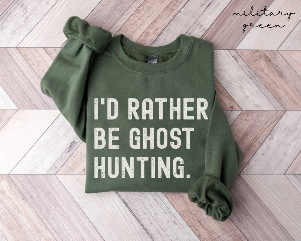 Military green sweatshirt with 'I'd Rather Be Ghost Hunting' text on a wooden floor.