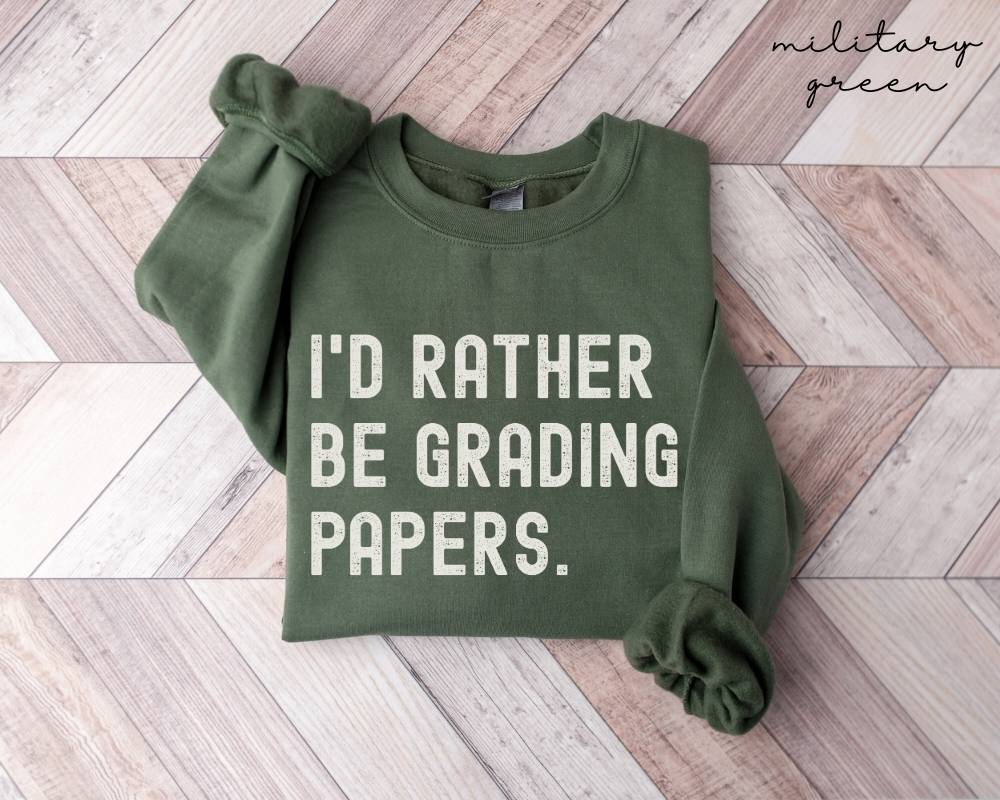 Military green sweatshirt with 'I'd Rather Be Grading Papers' text on a wooden floor.