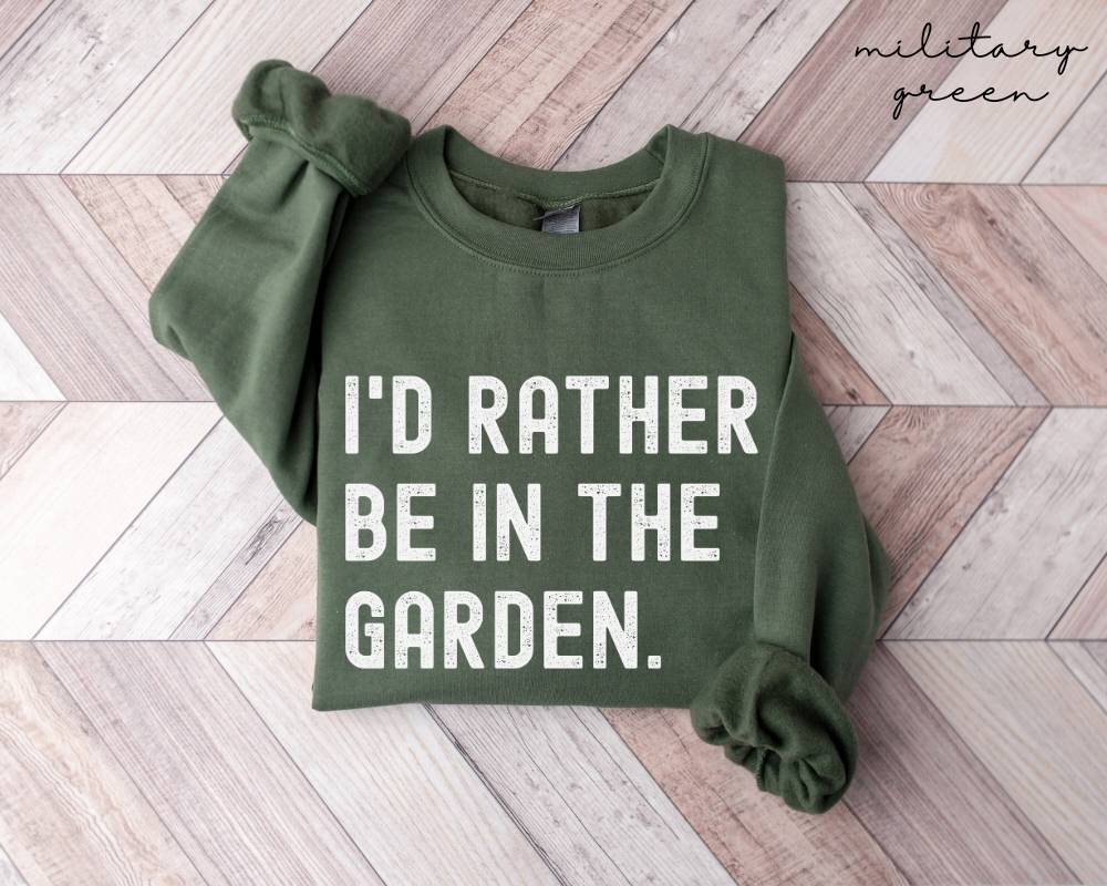 Military green sweatshirt with 'I'd rather be in the garden' text on a wooden floor.