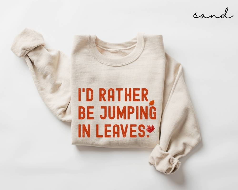 Beige (sand) sweatshirt with red text 'I'd rather be jumping in leaves' on a white background