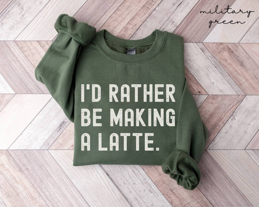 Military green sweatshirt with 'I'd rather be making a latte' text on a wooden floor.