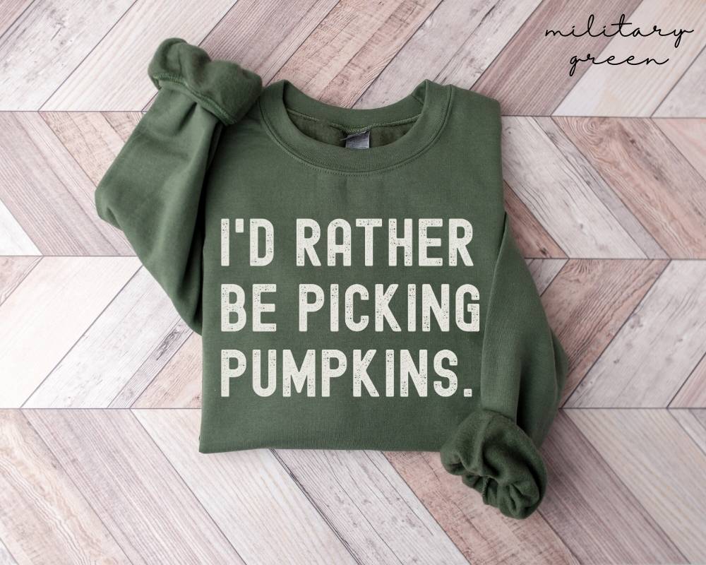 Military green sweatshirt with 'I'd Rather Be Picking Pumpkins' text on a wooden floor.