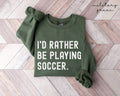 Military green sweatshirt with 'I'd rather be playing soccer' text on a wooden floor.