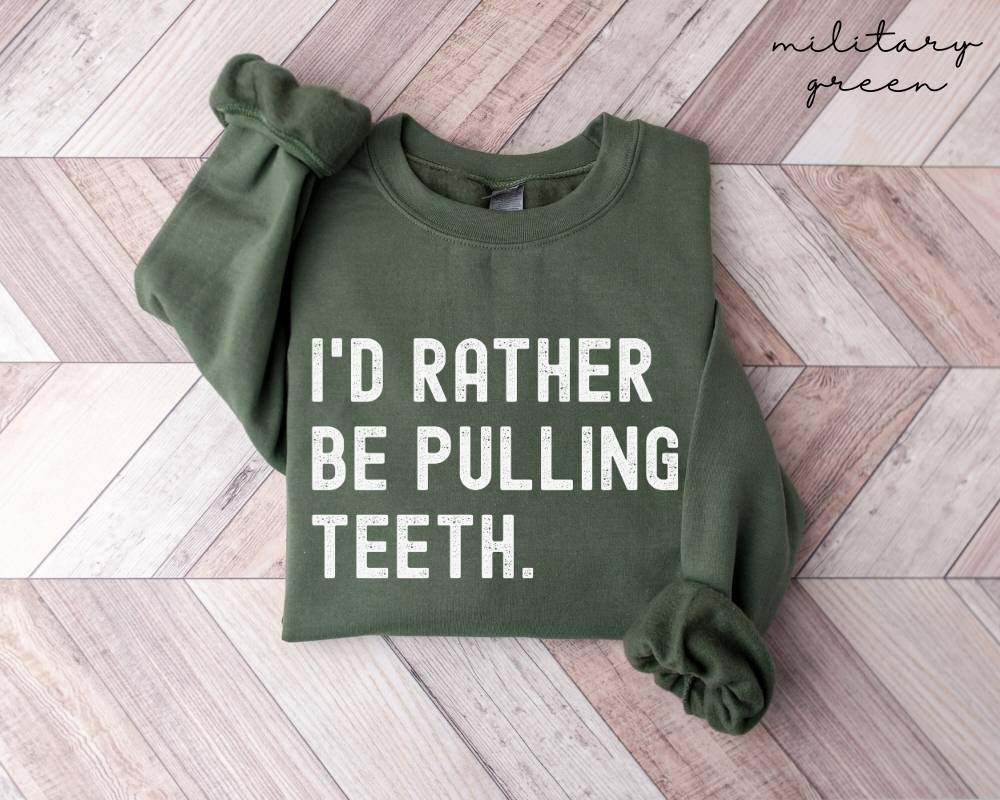 Military green sweatshirt with text 'I'd rather be pulling teeth' on a wooden floor.