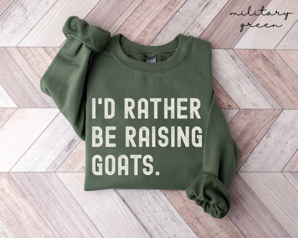 Military green sweatshirt with 'I'd Rather Be Raising Goats' text on a wooden floor.