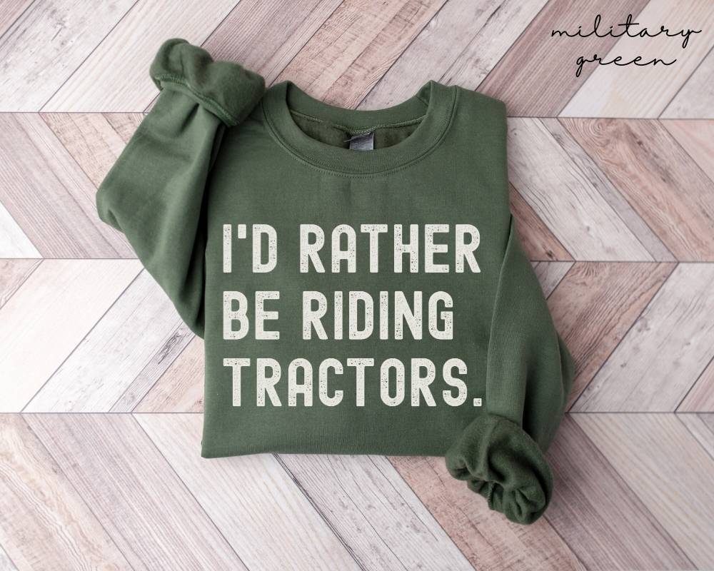 Military green sweatshirt with 'I'd Rather Be Riding Tractors' text on a wooden floor.