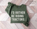 Military green sweatshirt with 'I'd Rather Be Riding Tractors' text on a wooden floor.