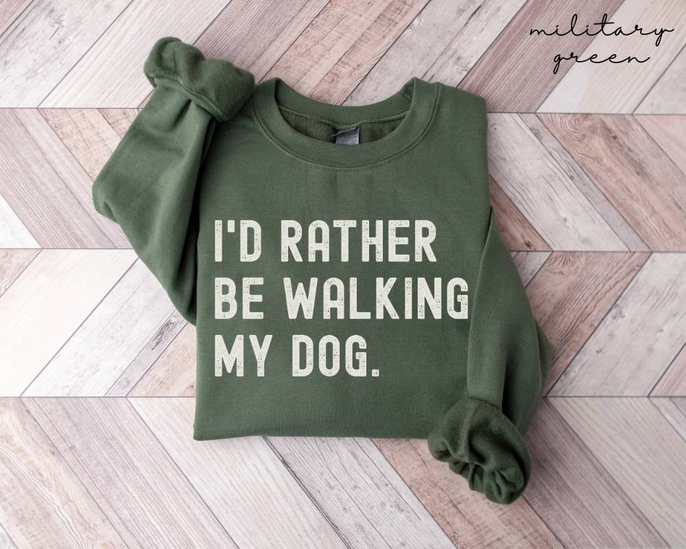 Military green sweatshirt with 'I'd Rather Be Walking My Dog' text on a wooden floor.