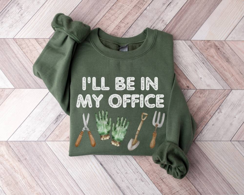 Military green sweatshirt with gardening-themed design and text on a wooden floor.