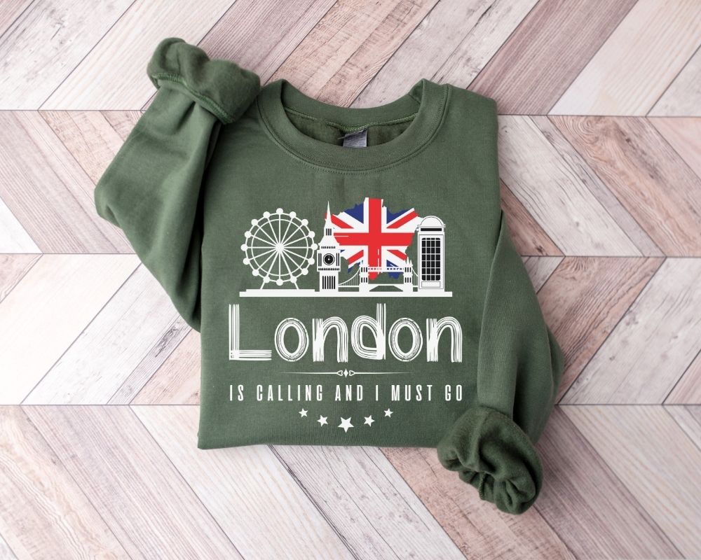 A military green sweatshirt featuring a London-themed design laid out on a wooden floor.