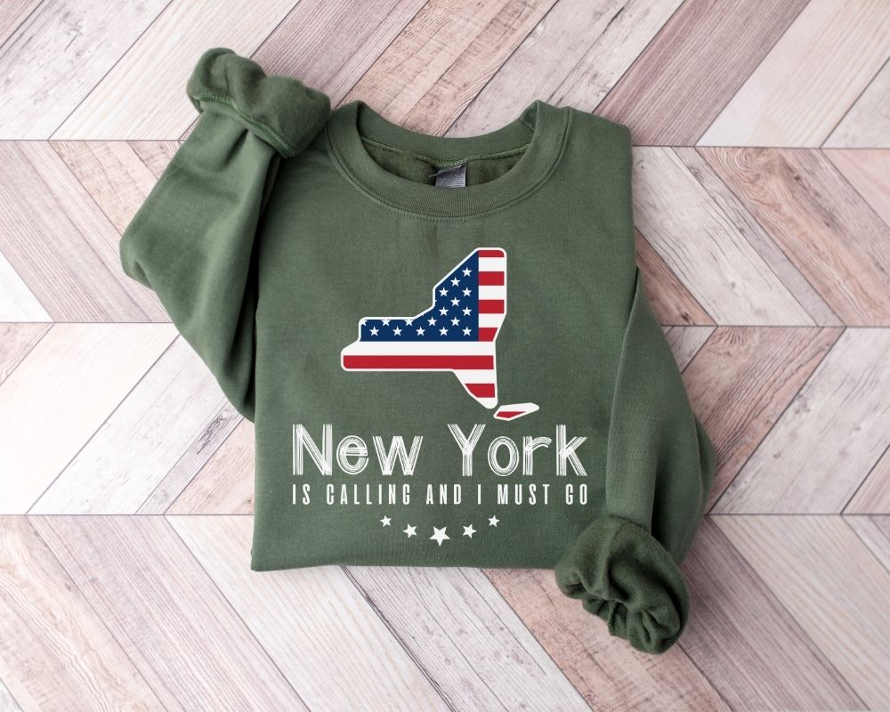 A millitray green sweatshirt featuring a New York design, placed on a wooden floor.