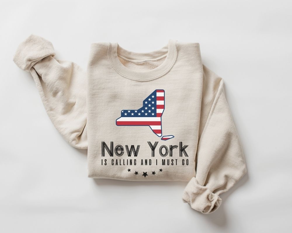 A beige (sand) sweatshirt featuring a design and text that represents New York, set against a white background.