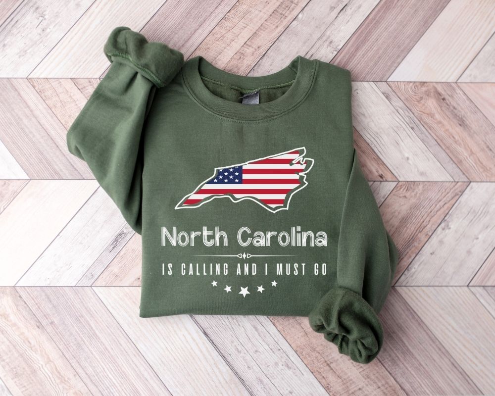 Military green sweatshirt with North Carolina design and text on a wooden floor