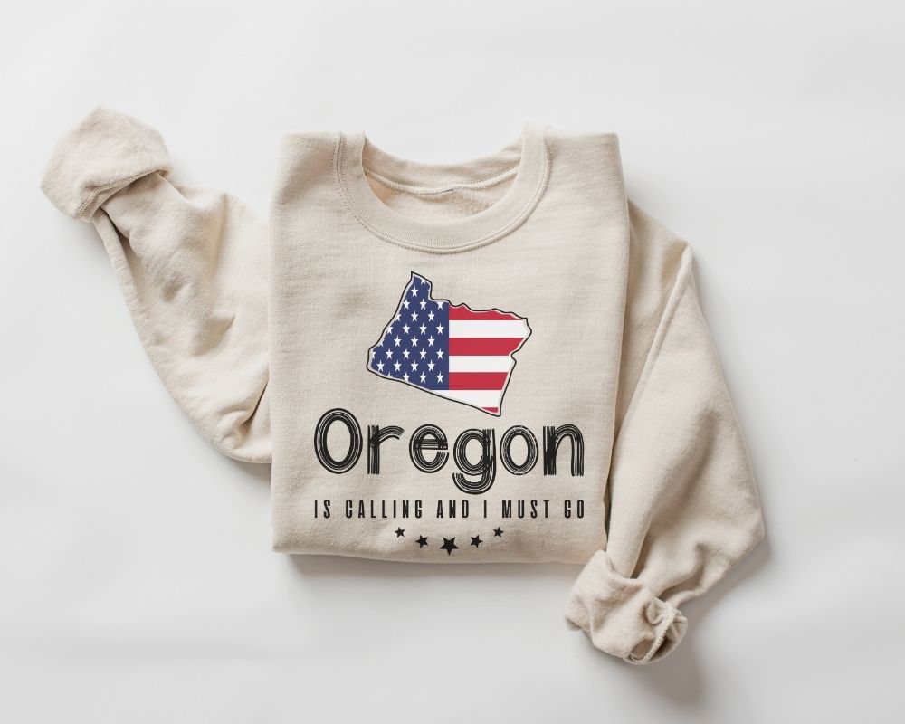 A beige (sand) sweatshirt featuring the American flag and the text "Oregon" on a white background.