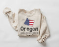 A beige (sand) sweatshirt featuring the American flag and the text "Oregon" on a white background.