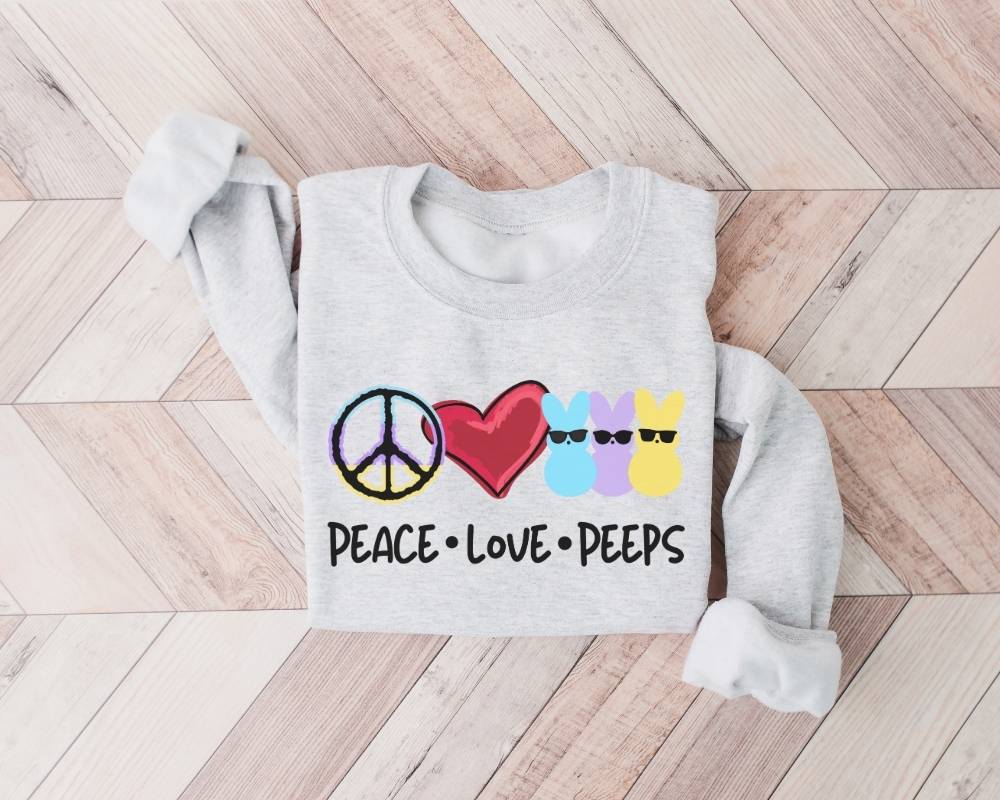 Gray (ash) sweatshirt with peace, love, and peeps design on a wooden floor