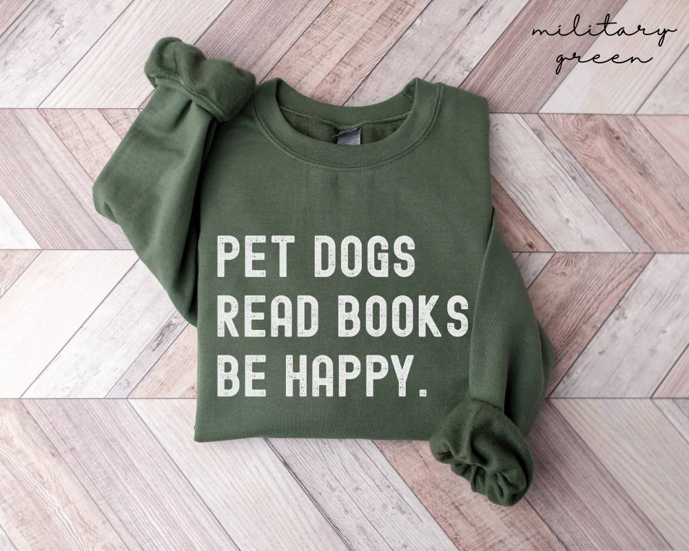 Military green sweatshirt with text 'PET DOGS READ BOOKS BE HAPPY' on a wooden floor.