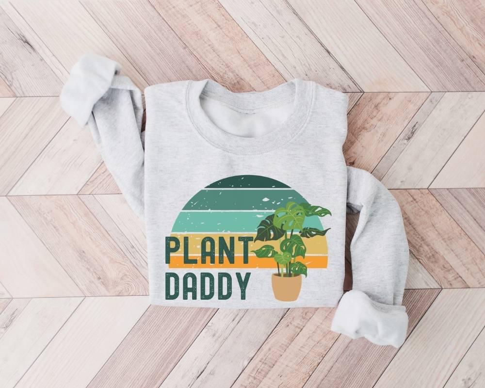 White (ash) sweatshirt with 'Plant Daddy' graphic on a wooden floor