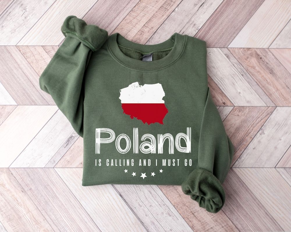 A millitray green sweatshirt featuring a design of the Polish flag and text, laid out on a wooden floor.
