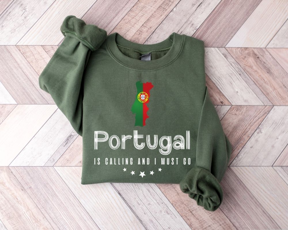 A millitray green sweatshirt featuring a design and text related to Portugal, laid out on a wooden floor.