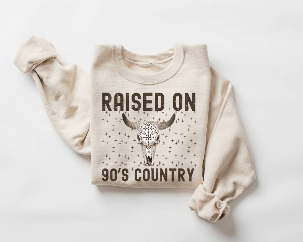 Beige (sand) sweatshirt with 'Raised on 90's Country' text and bull skull design on a white background
