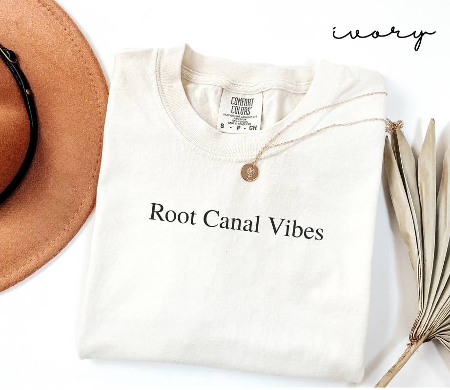 White (ivory) t-shirt with 'Root Canal Vibes' text, brown hat, and dried plant on a white background