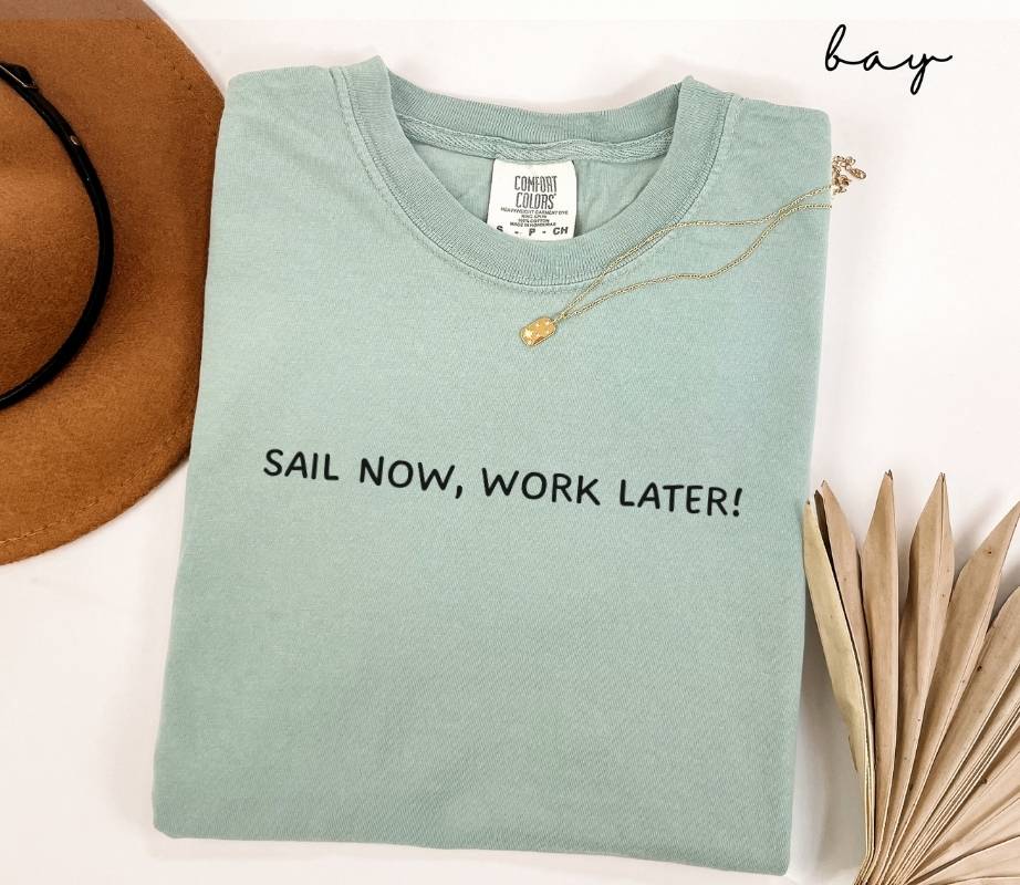 Folded light green (bay) t-shirt with 'Sail Now, Work Later!' text on a white background.