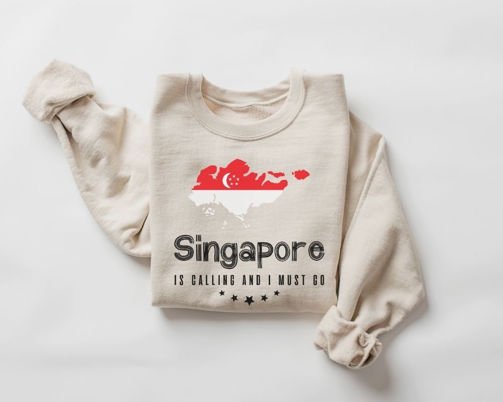 A beige (sand) sweatshirt featuring a design and text related to Singapore on a white background.