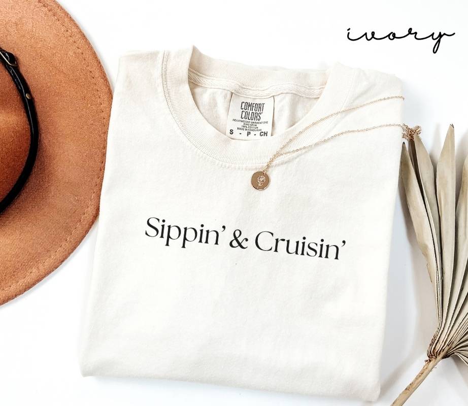 White (ivory) t-shirt with 'Sippin' & Cruisin'' text, brown hat, and dried plant on a white background
