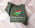 A military green sweatshirt featuring a design of the South African flag and text placed on a wooden floor.