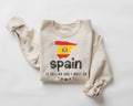 Beige (sand) sweatshirt featuring the Spanish flag along with text, displayed on a white background.