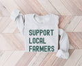 Ash (Gray) sweatshirt with 'Support Local Farmers' retro dark green text on a wooden floor