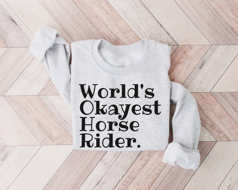 Gray (ash) sweatshirt with 'World's Okayest Horse Rider' text on a wooden floor
